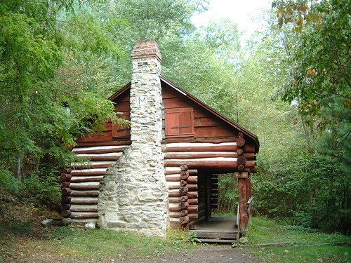 The side view of the Milesburn Cabin shows a stone chimney and wooden side paneling.