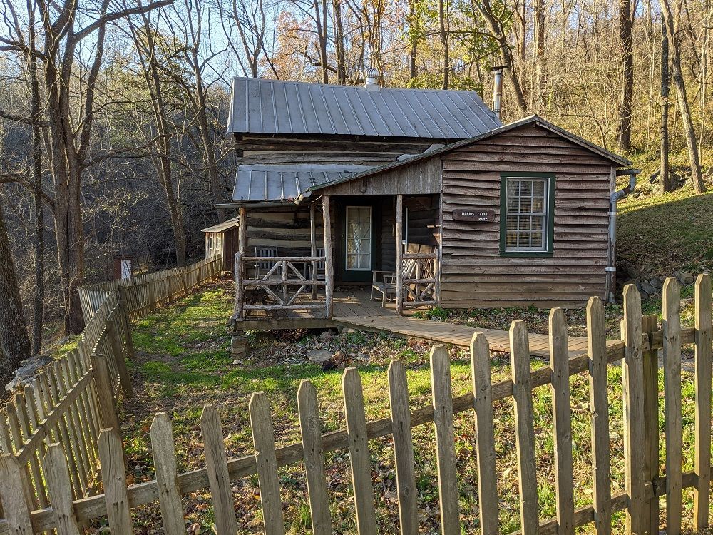 The front view of Morris Cabin shows a wooden fence surrounding the cabin, leading to a walkway and wooden porch.
