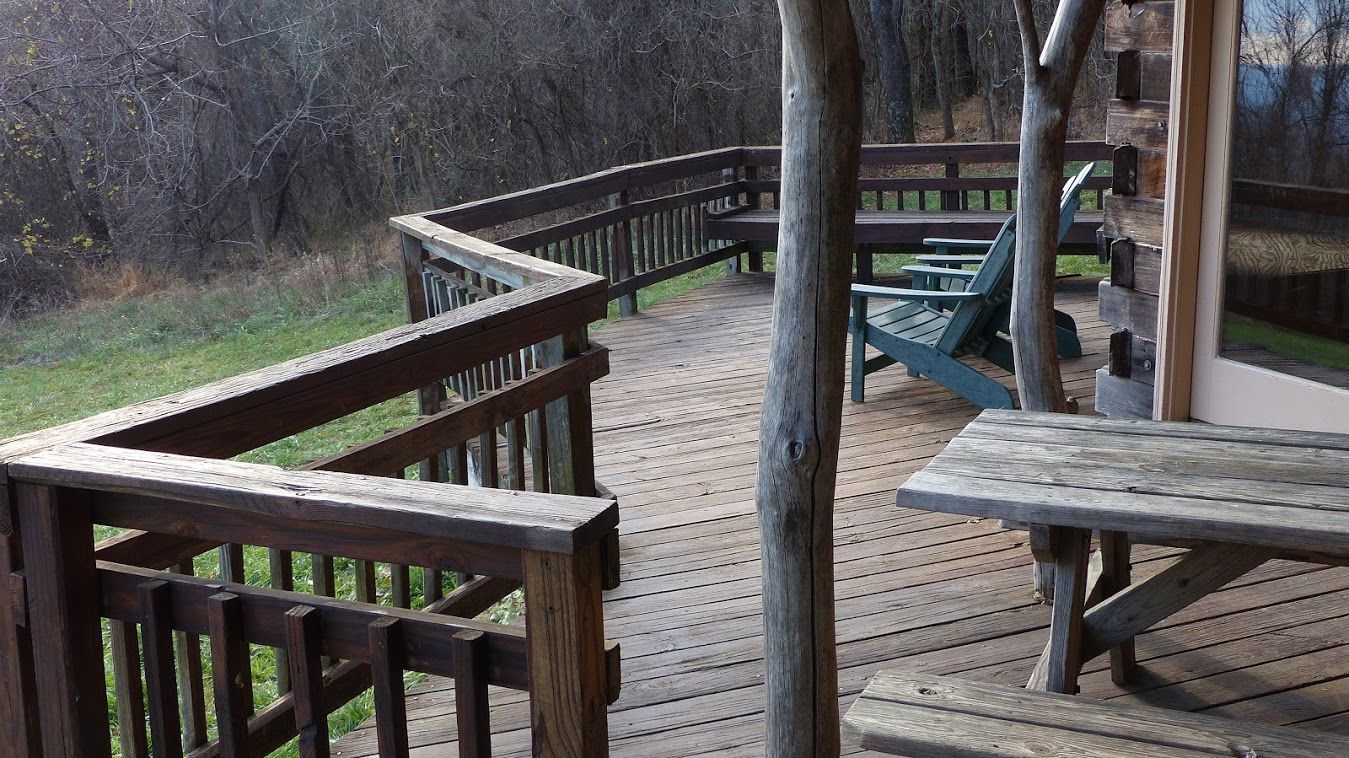 The wooden porch on Mutton Top cabin shows many wooden chairs and wooden picnic tables. 