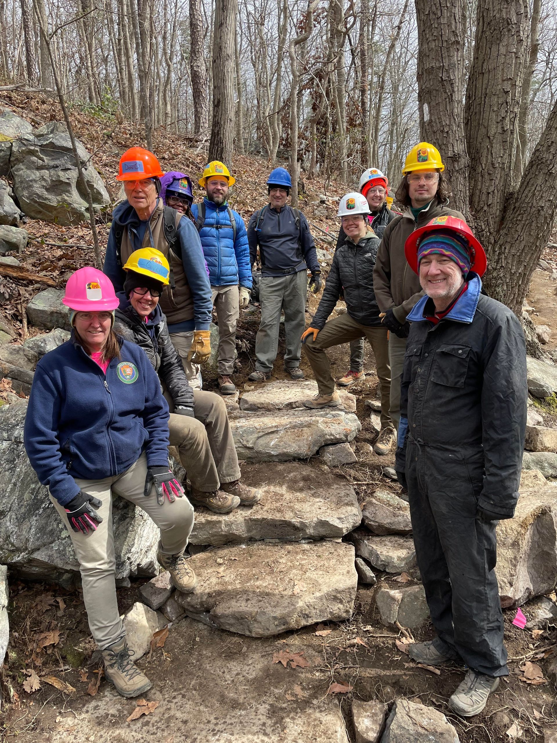 A group of people wearing hard hats are standing next to each other in the woods.