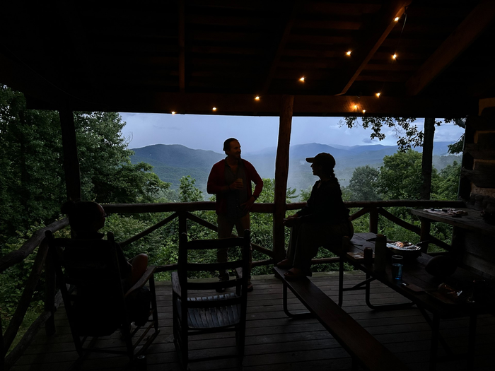 A man and a woman are sitting on a porch overlooking mountains.