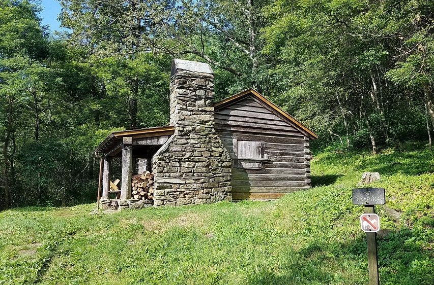 The side of the Pocosin cabin shows a stone chimney and firewood. 