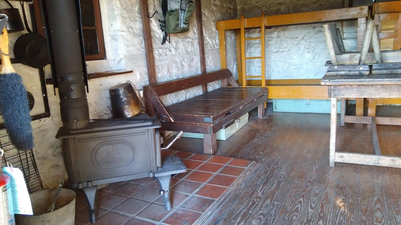 The interior of the range view cabin shows a fireplace, a wooden bed, and a small table.