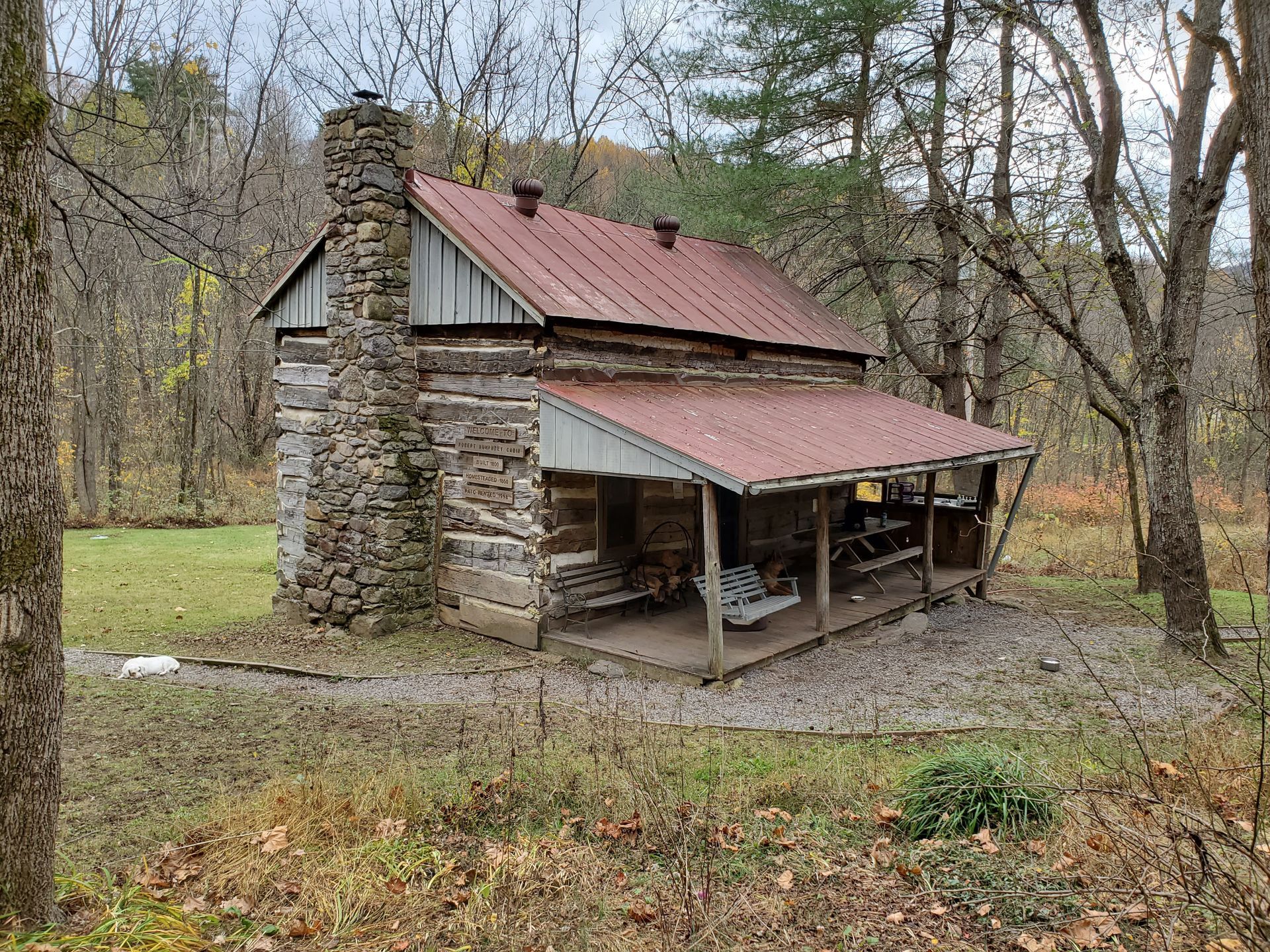The front view of Robert Humphrey's cabin shows a wooden porch with hanging benches and a wooden picnic table.