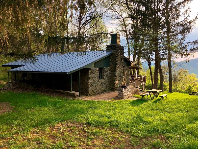 The side view of the Schairer Cabin shows a small front and back porch, and a wooden picnic table in the grass.