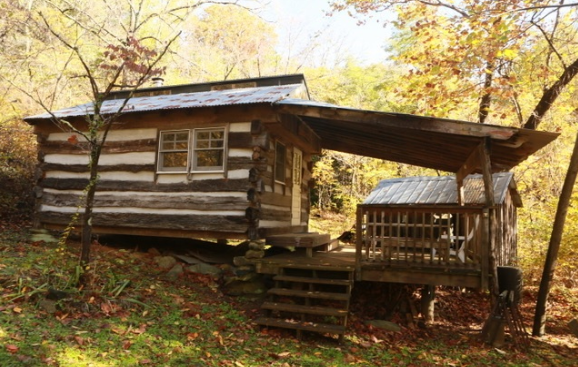 The side view of Butternut cabin showing a wooden staircase leading to a wooden porch with chairs.