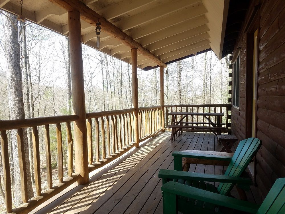 The front porch of the Silberman Trail Cabin features green wooden chairs and a wooden picnic table.