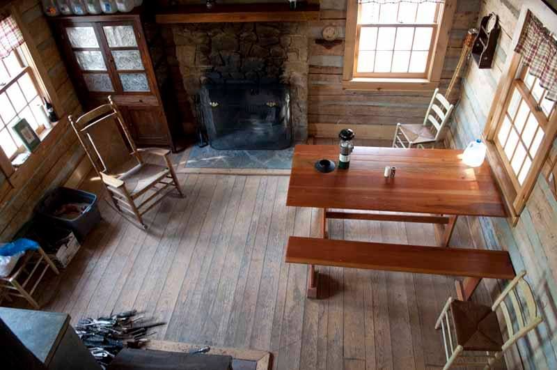 The interior of Tulip Tree cabin shows a wooden table and bench, with multiple wooden chairs.