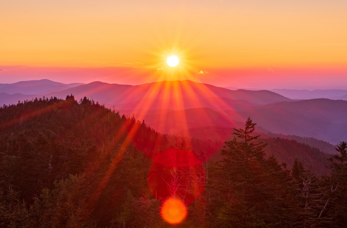 A pink, yellow, and orange sunrise atop a mountainous valley.