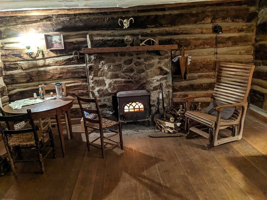 The interior of vining cabin showing a small fireplace, wooden table and chairs, and a wooden rocking chair.
