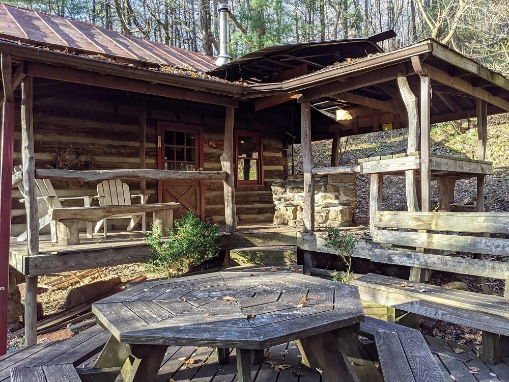 The side view of Wineberry cabin shows a wooden porch and wooden seating area with a table and benches..