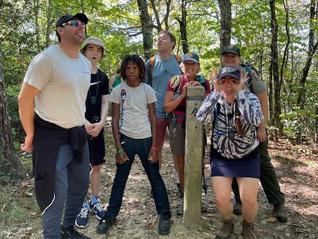 A group of people are standing around a post in the woods.