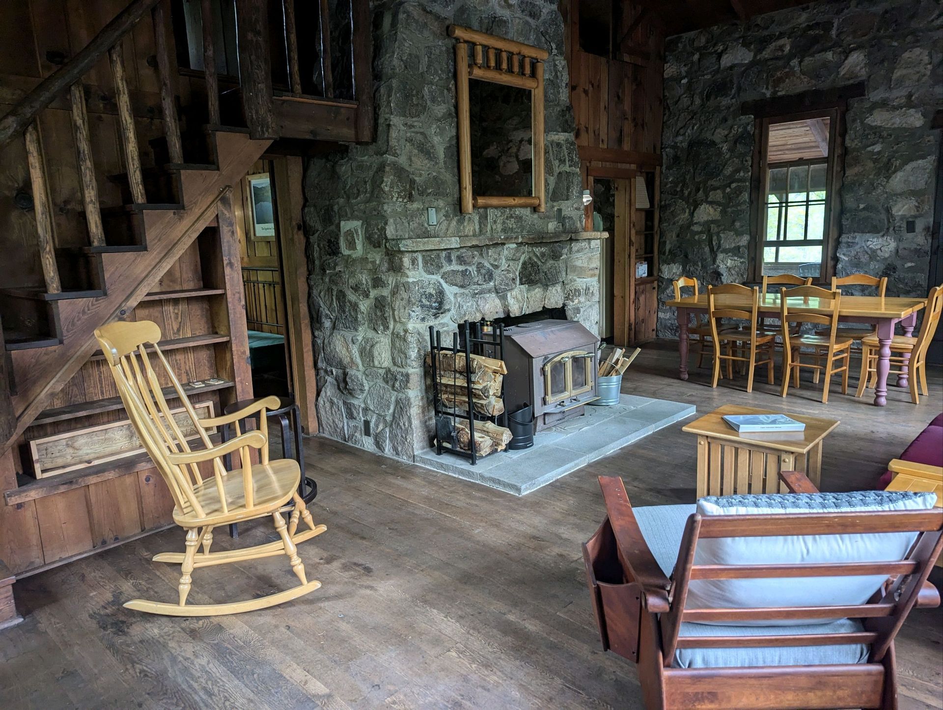 The interior of Tulip Tree cabin shows a wooden table with multiple wooden chairs, and a stone fireplace with a wood burning stove.