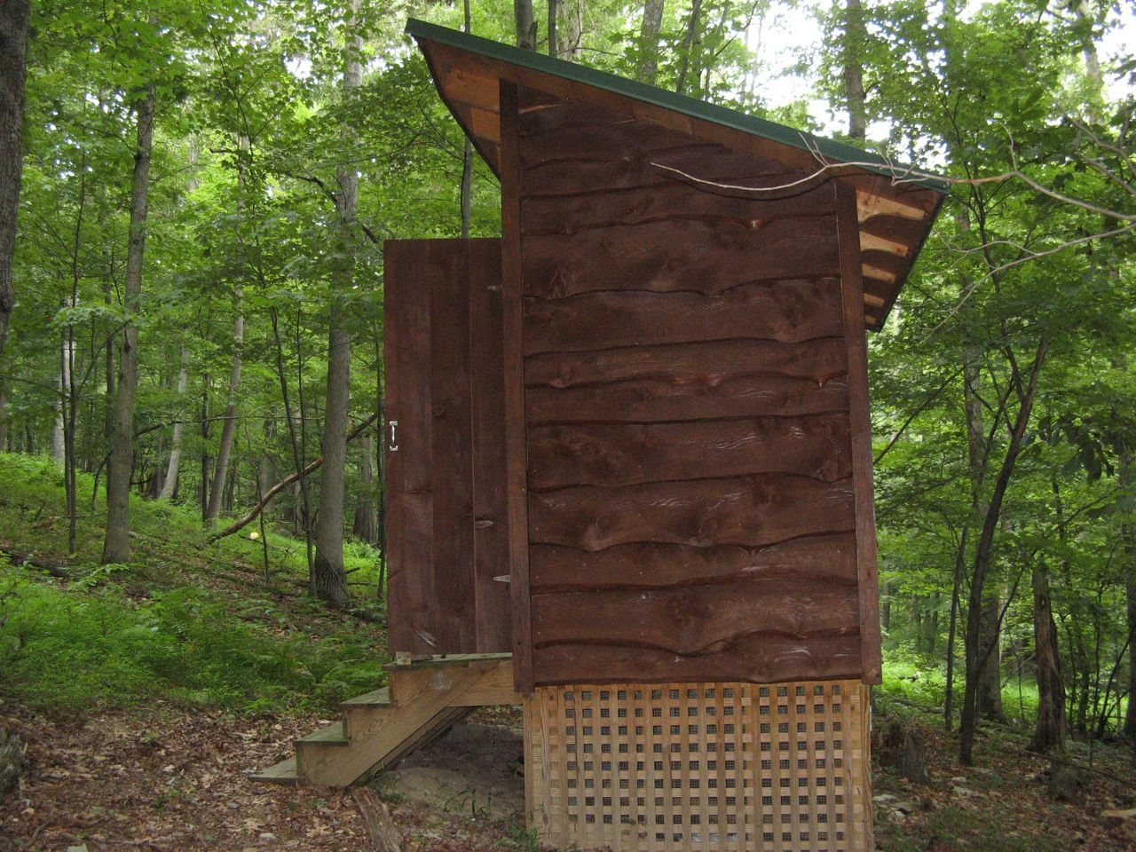 A wooden outhouse is sitting in the middle of a forest.