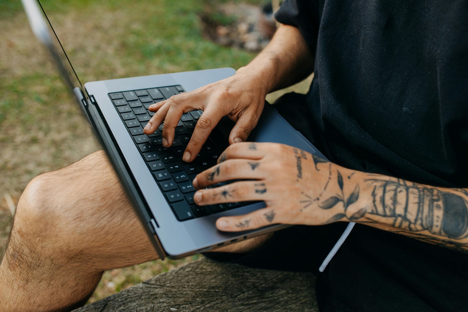 A man with tattoos is typing on a laptop computer.
