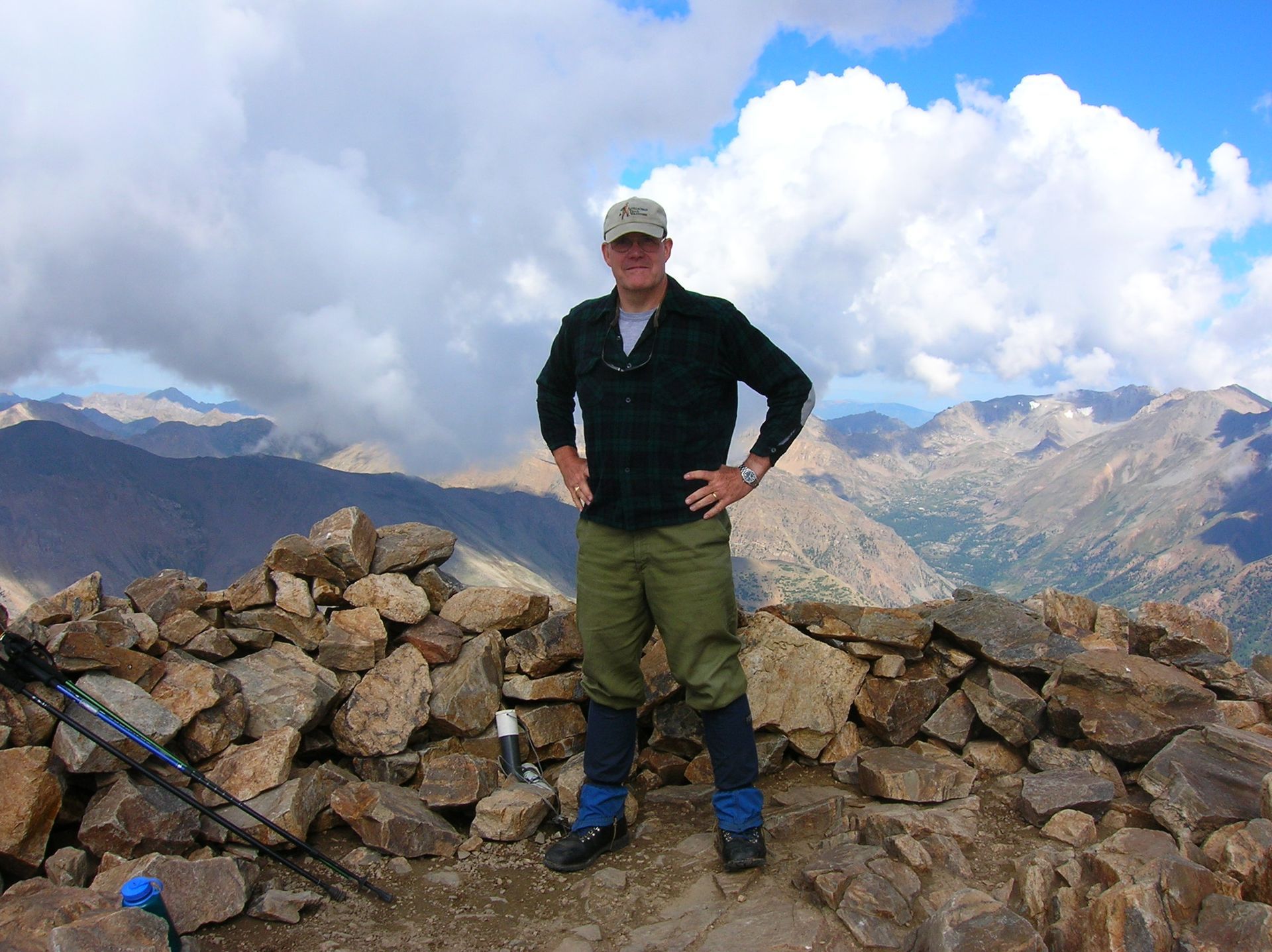 Rush standing on a rocky summit wearing a dark plaid shirt