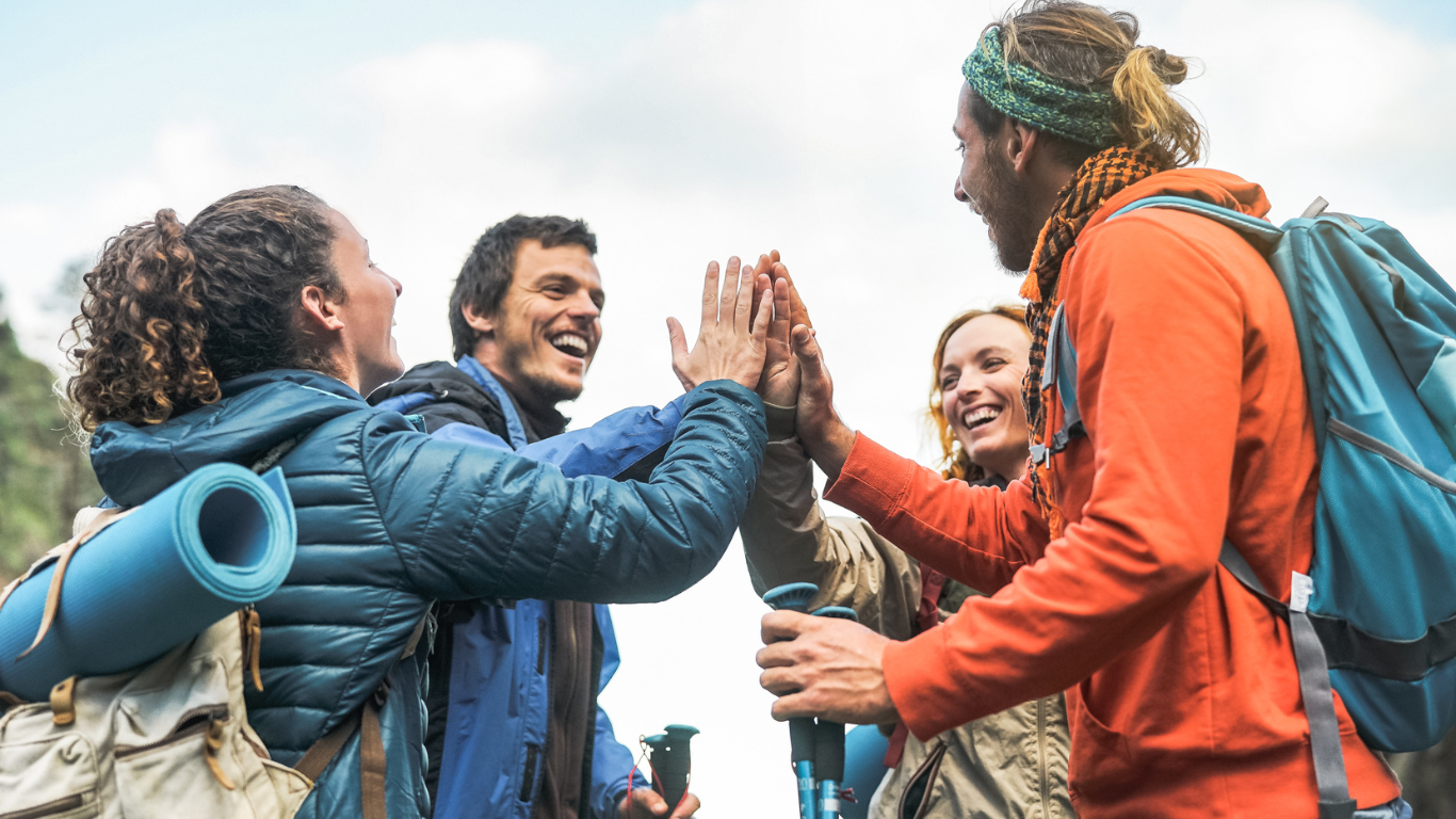 A group of hikers high-fiving each other, wearing backpacks and holding hiking gear.