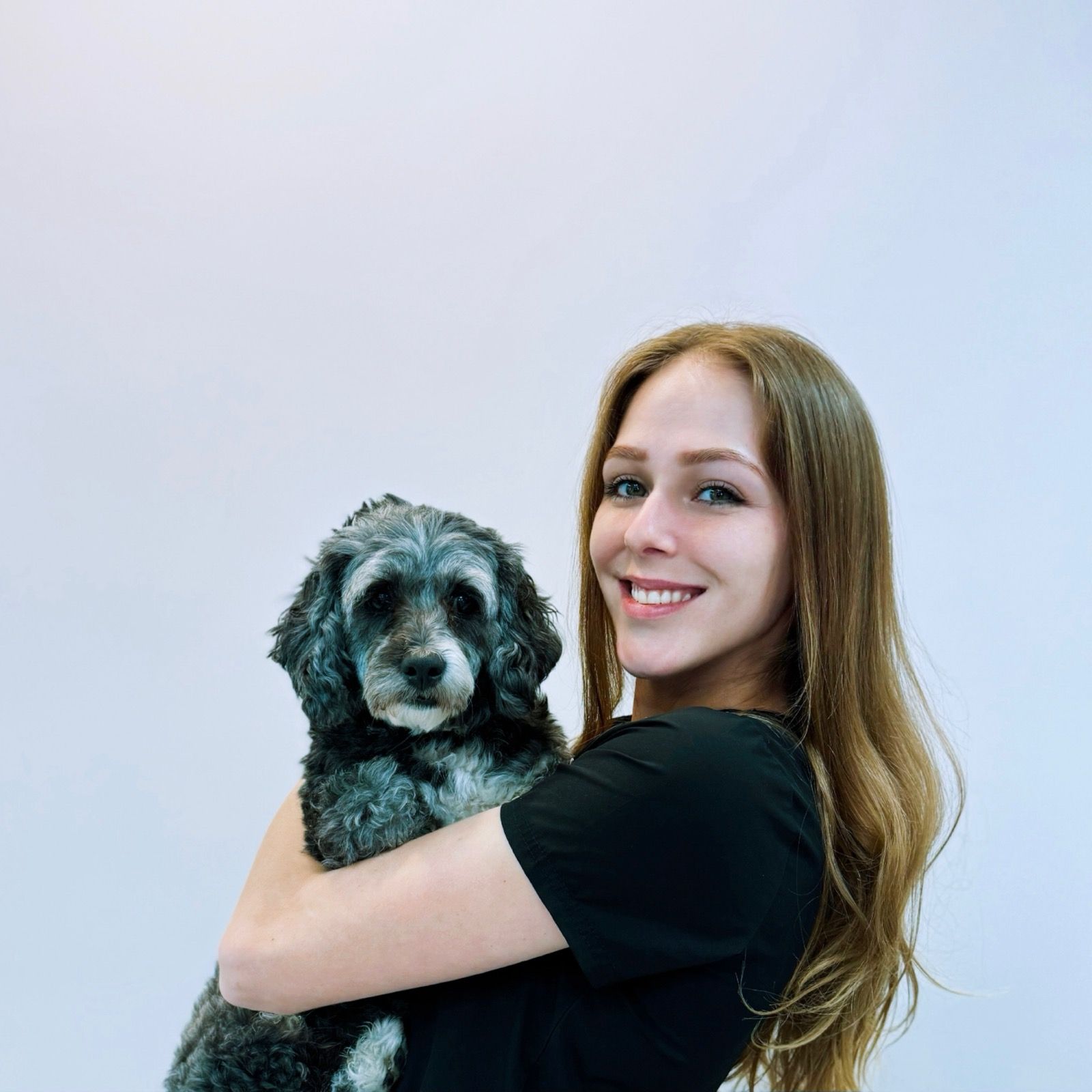 A woman in a black shirt is holding a small dog