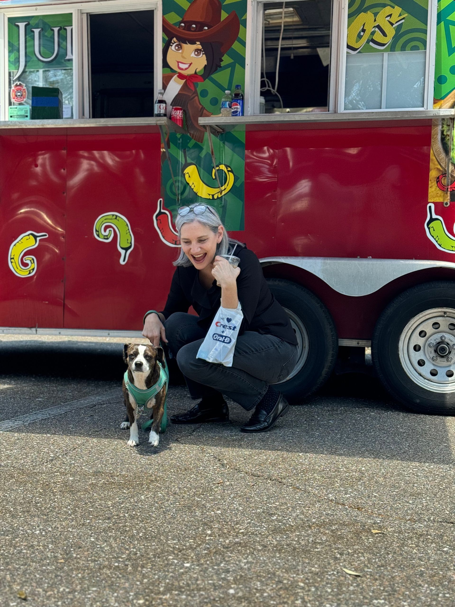A woman is kneeling down next to a dog in front of a food truck.