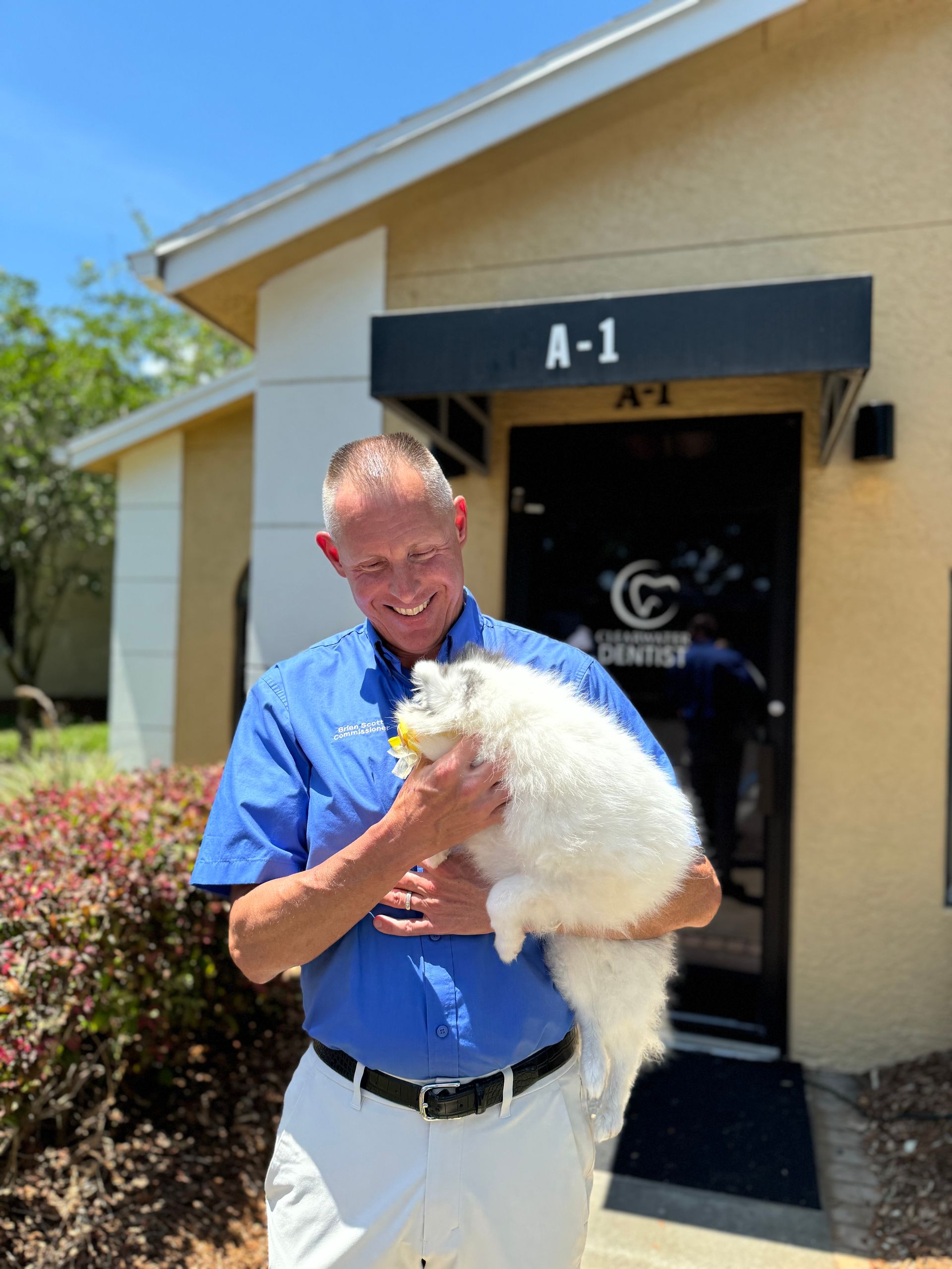 A man is holding a white cat in front of a building with the number a-1 on it