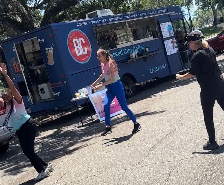 Two women are dancing in front of a blue food truck.
