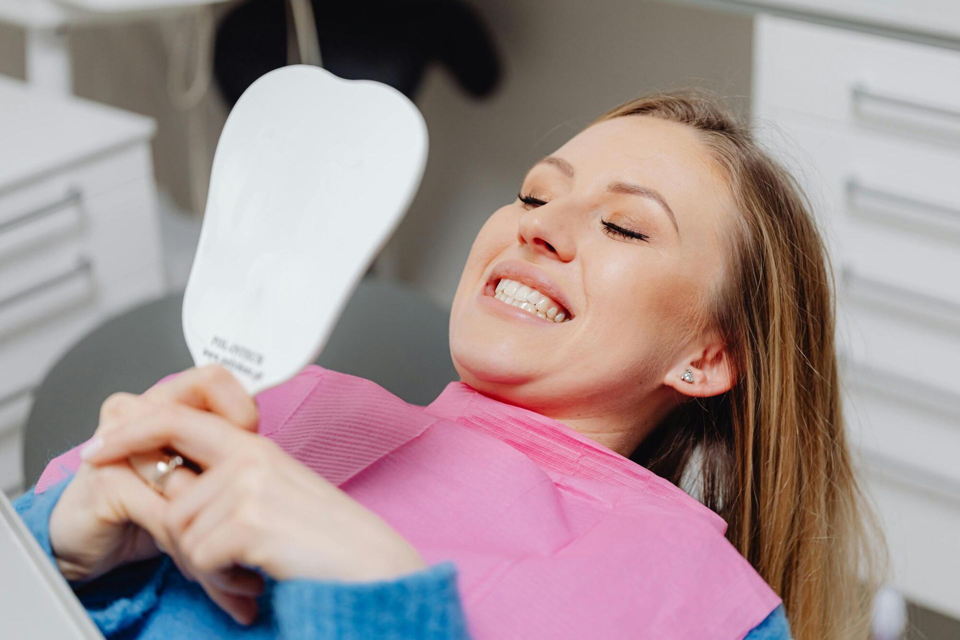 A woman is sitting in a dental chair looking at her teeth in a mirror.