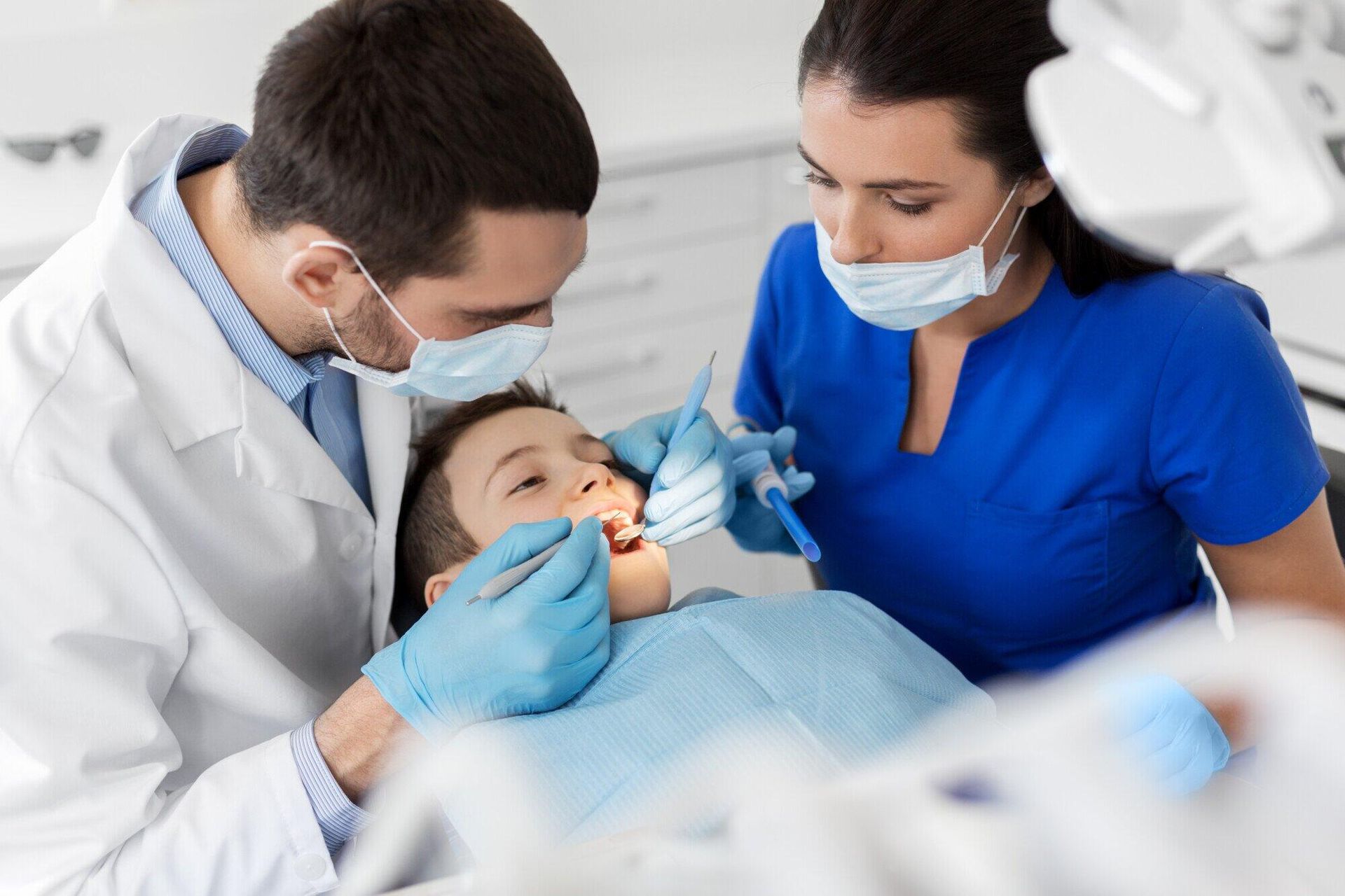 A young boy is getting his teeth examined by two dentists.