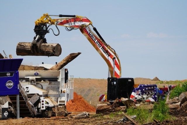 A large excavator is loading a log into a machine