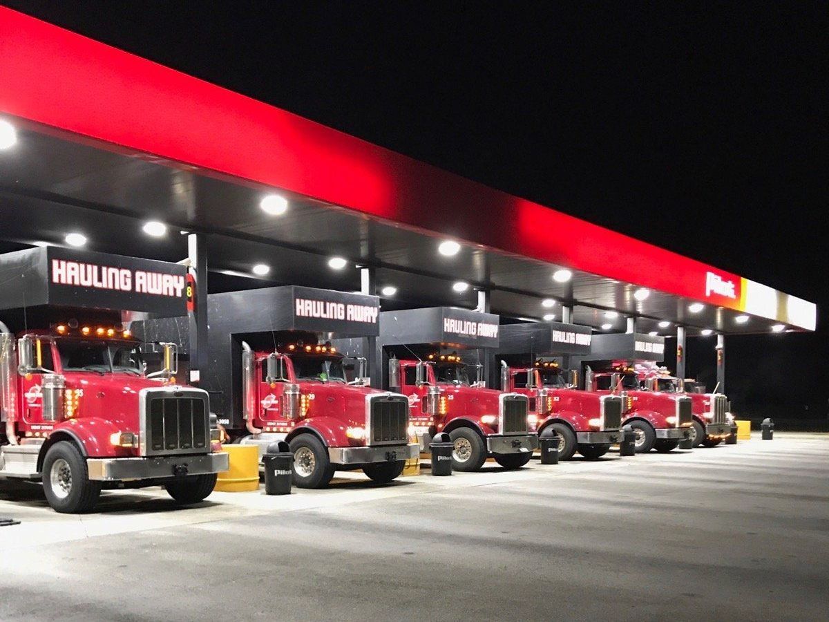 A row of red trucks are parked at a gas station at night.