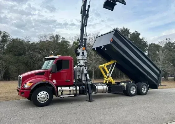 A red dump truck with a crane attached to it is parked on the side of the road.