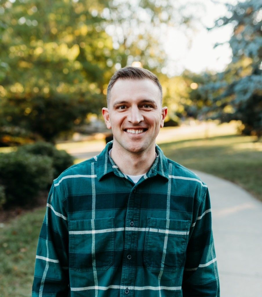 A man in a suit is standing on a sidewalk with his arms crossed.