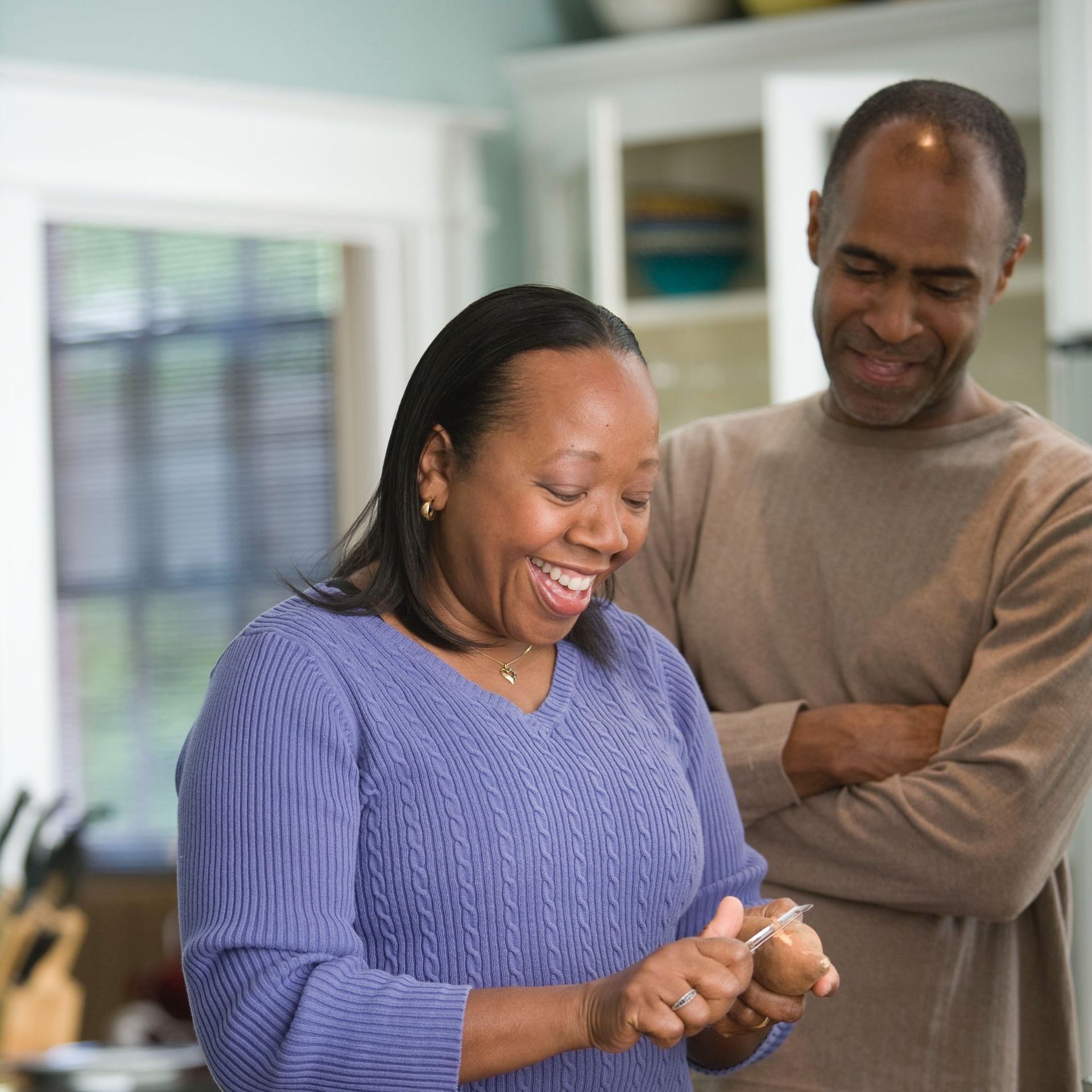 A woman in a blue sweater is smiling while standing next to a man in a kitchen.