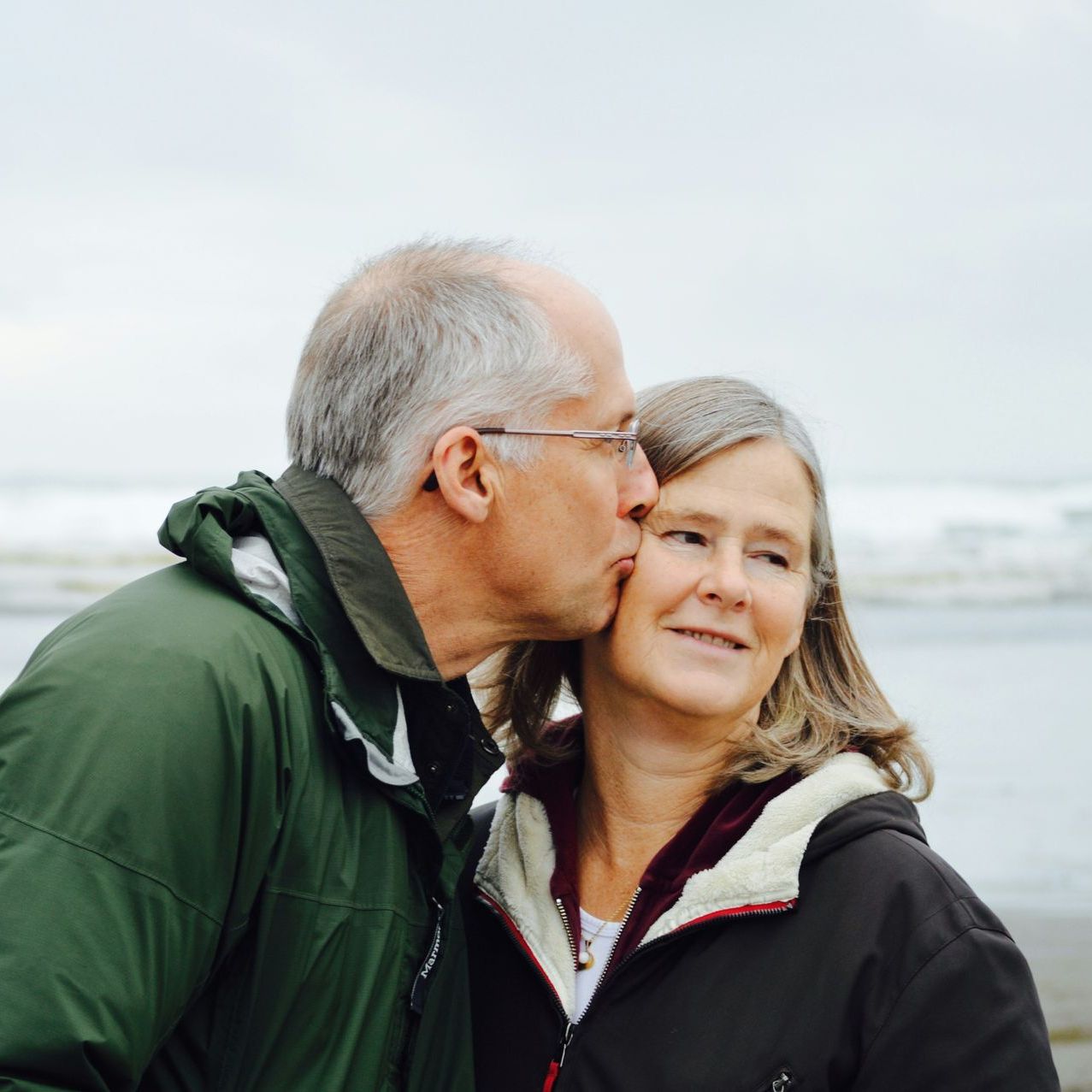 A man in a green jacket kisses a woman on the cheek