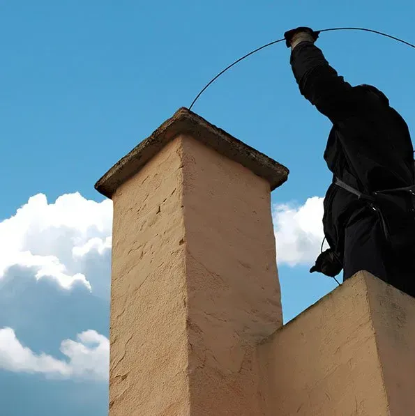A man is standing on top of a chimney holding a hose
