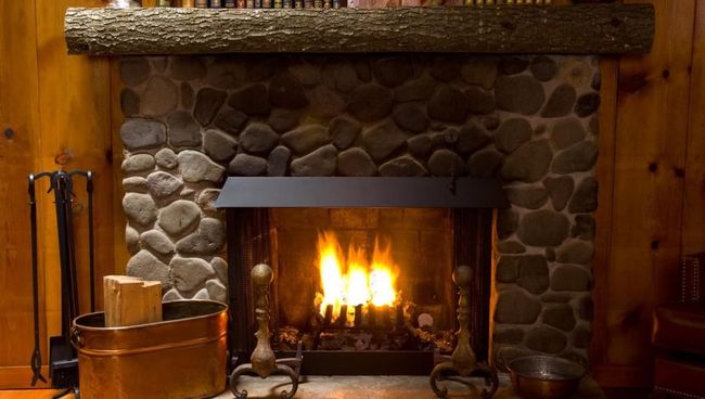 A stone fireplace with a log on the mantle is lit up in a living room.