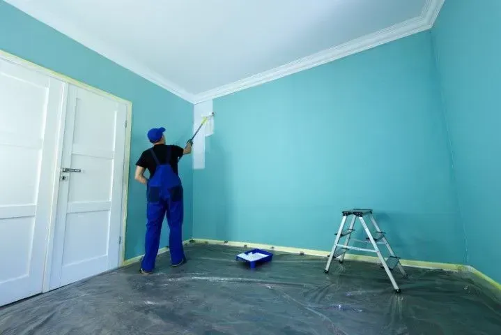 Painter using a roller on a vibrant teal interior wall.