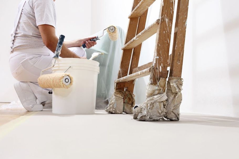 Painter prepping a room with drop cloths and a ladder.