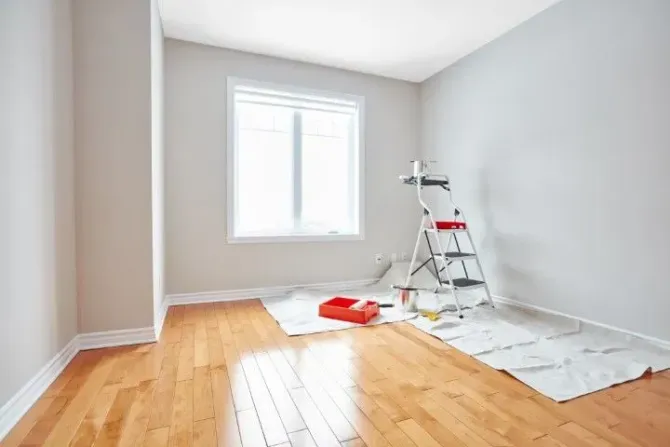 Brightly lit room with painting tools and a ladder on a drop cloth.