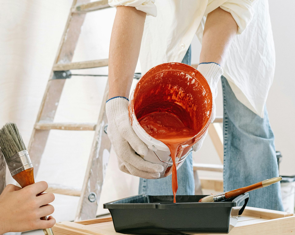 Professional painter pouring bright orange paint into a bucket.