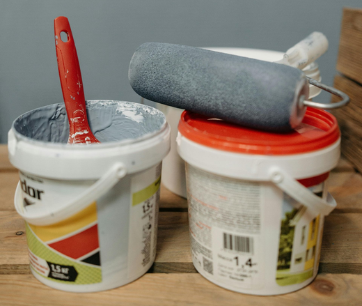 Close-up of paint buckets and a loaded roller with grey paint.