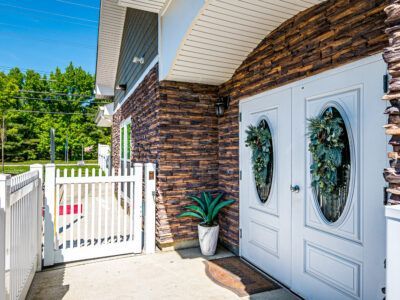 The front door of a brick house with white doors and a white gate.