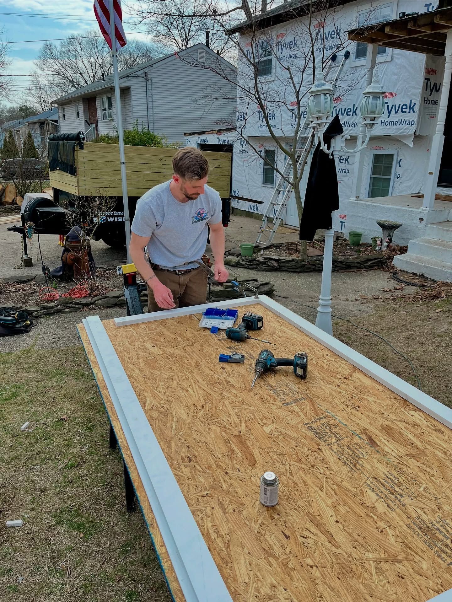 Man working on a wooden door on a workbench outside a house under construction.