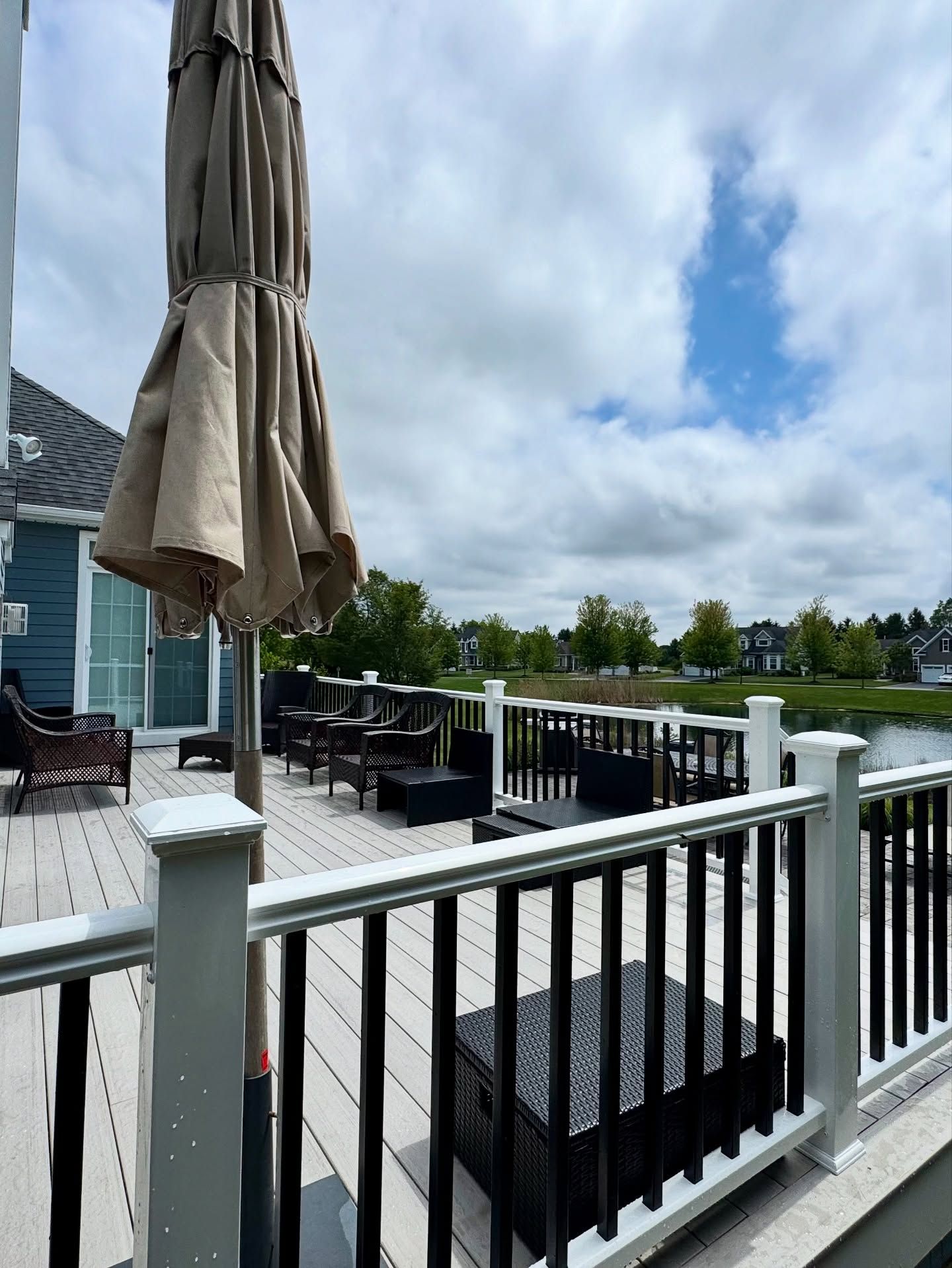 Deck with a closed umbrella, outdoor furniture, and view of a lake and sky.