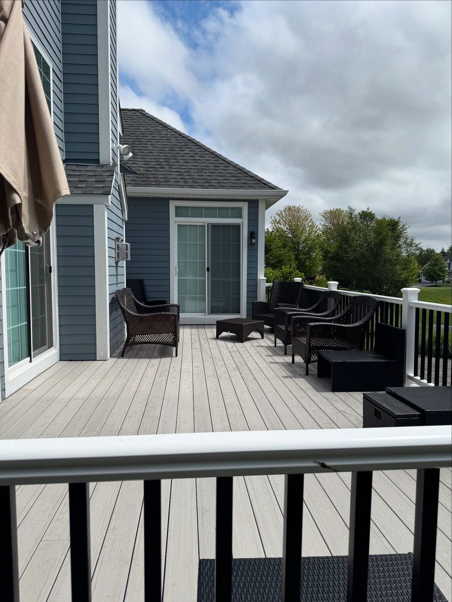 Wooden deck with outdoor furniture next to a blue house on a cloudy day.