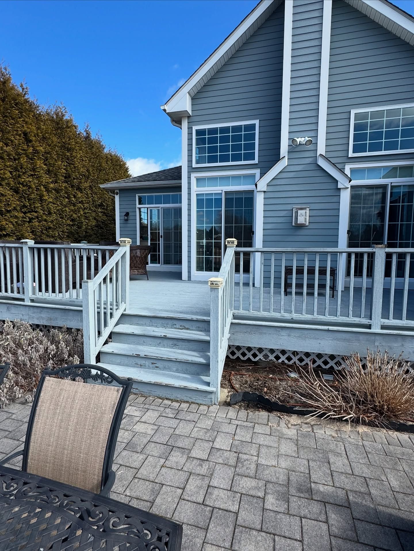 Deck with stairs leading up to a two-story house with blue siding and large windows, sunny day.