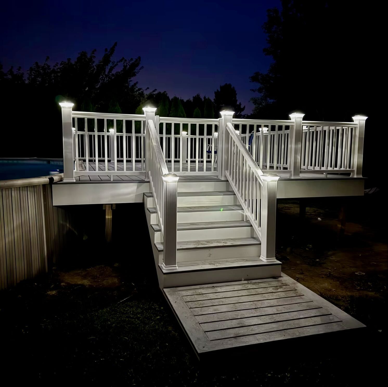 Lit deck at night, with stairs and ramp, white railings with lights, against a dark sky.