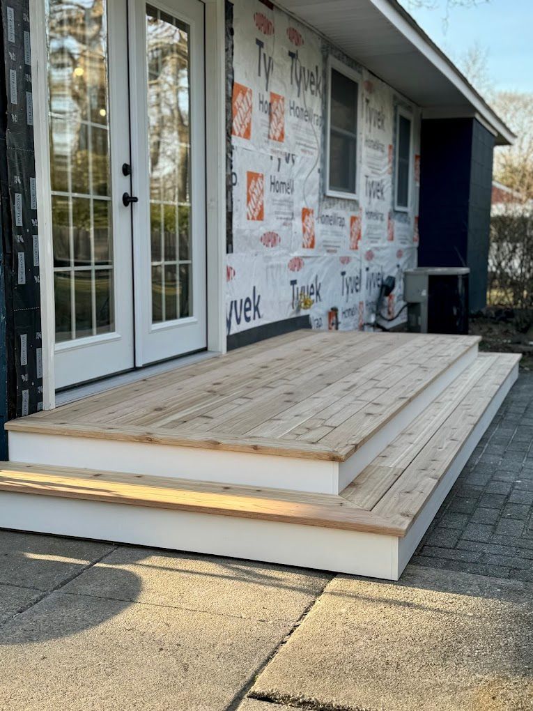 Newly built wooden deck with steps in front of a house, French doors visible.