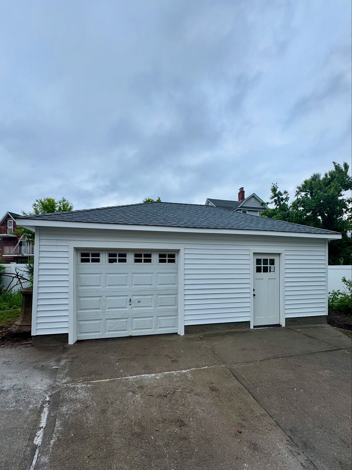 White garage with gray roof and door on a concrete driveway under a cloudy sky.