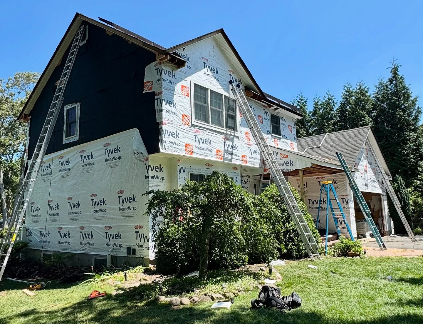 House under construction, covered in Tyvek wrap, with ladders propped against the siding.