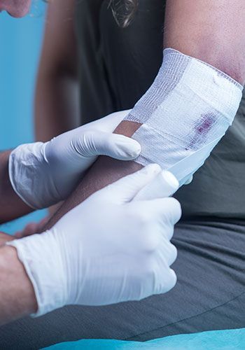 Person with bandaged elbow, being attended to by someone in gloves.